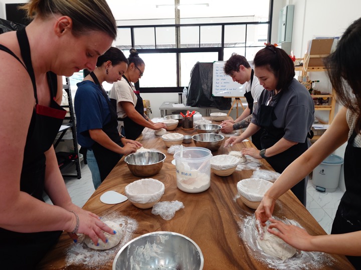 Guests kneading dough together along the long wooden studio table