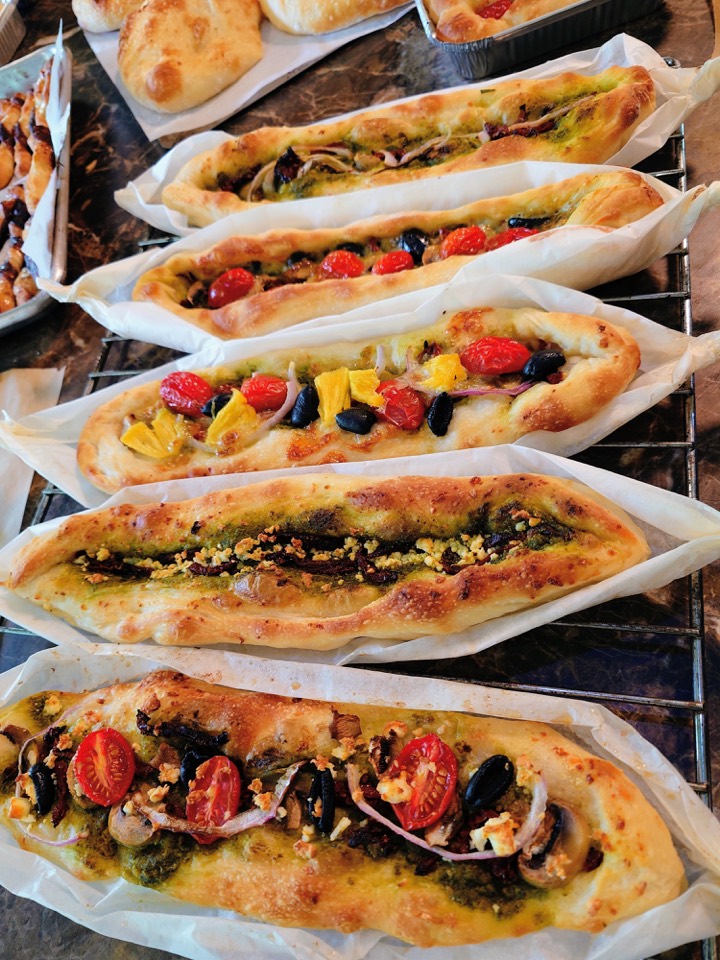 Boat-shaped flatbreads topped with pesto, tomatoes, olives and peppers on a cooling rack