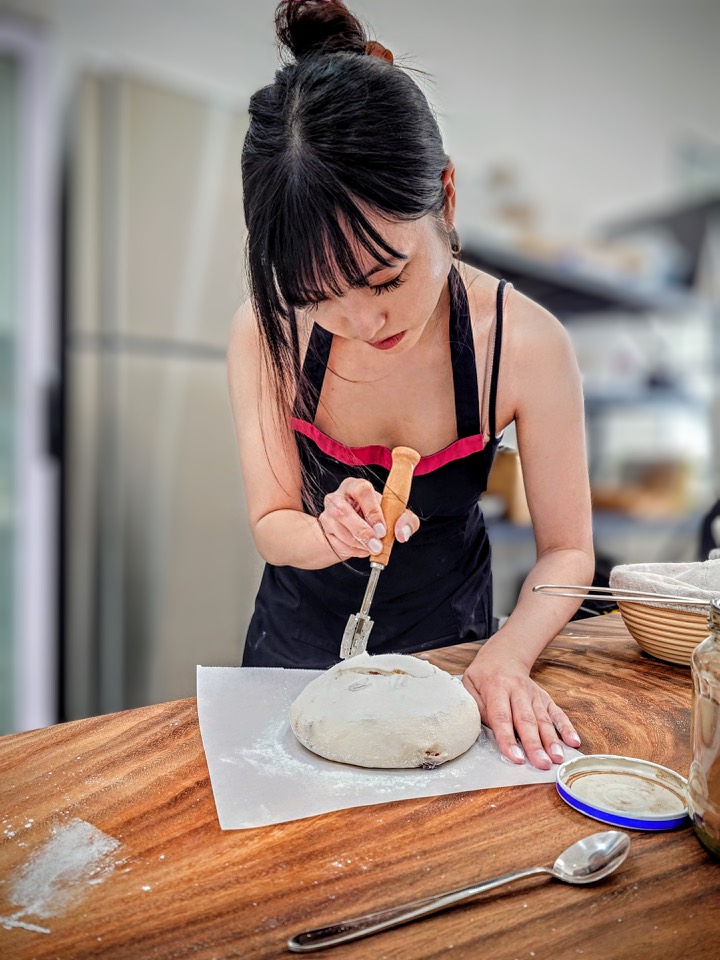 A baker scoring a round loaf with a lame