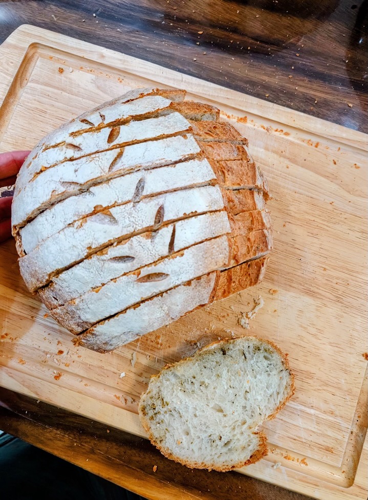 A hand-scored sourdough loaf, sliced on a wooden board, with one slice showing the open crumb