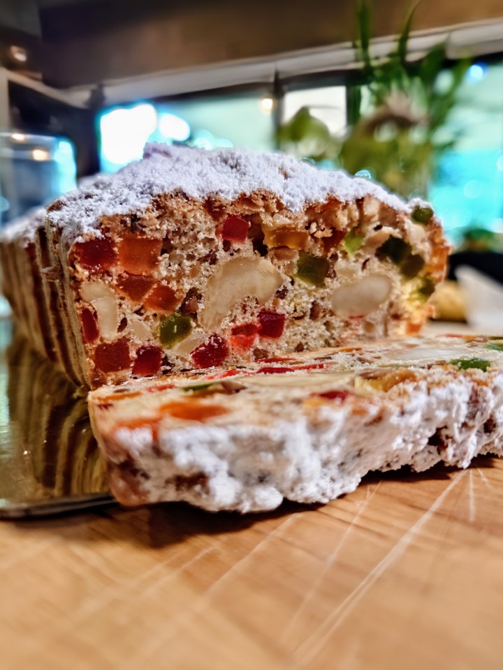 A sliced Christmas stollen full of candied fruit and nuts, dusted with icing sugar